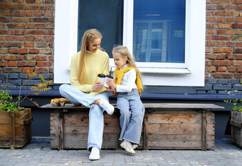 Mom and daughter are sitting on a bench with glasses of hot chocolate and croissants. The family spends the weekend together.