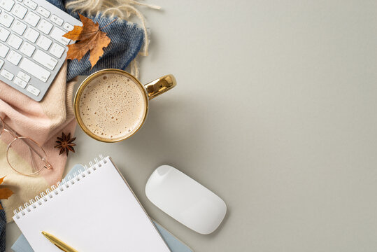 Autumn-themed workplace at home. Top view image of keyboard and mouse, notepad, pen, mug of coffee, cashmere scarf, autumnal decorations with space for promotion on grey isolated background