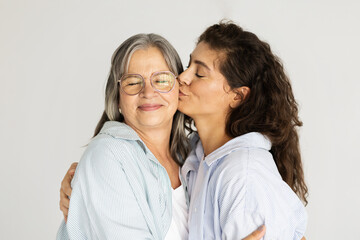 Cheerful mature woman hugging and kissing on cheek of old lady, enjoy mom daughter visit