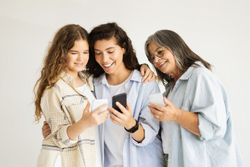 Happy millennial, senior women and teen girl hug, enjoy chat on smartphone