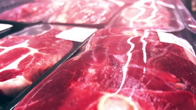 Raw fillets or steaks of pork or beef in plastic containers covered with cling-wrap in a supermarket refrigerator. Close-up shot