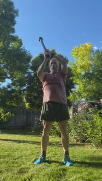 senior, athletic man is exercising in a backyard with a steel mace by doing 360 rotation, green summer scenery