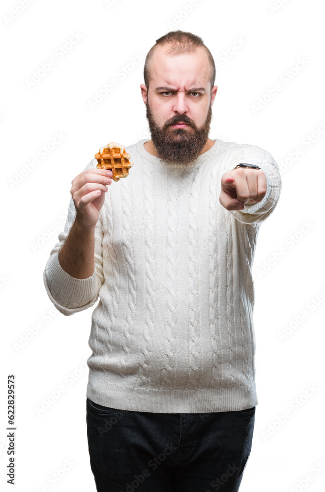 Sticker Young caucasian hipster man eating sweet waffle over isolated background pointing with finger to the camera and to you, hand sign, positive and confident gesture from the front