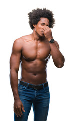 Fototapeta premium Afro american shirtless man showing nude body over isolated background smelling something stinky and disgusting, intolerable smell, holding breath with fingers on nose. Bad smells concept.