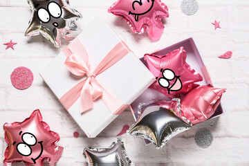 Gift box and balloons with drawn cute faces on light background