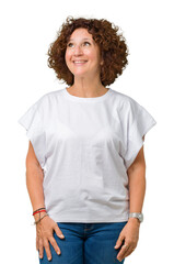 Beautiful middle ager senior woman wearing white t-shirt over isolated background smiling looking side and staring away thinking.