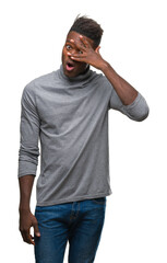 Fototapeta premium Young african american man over isolated background peeking in shock covering face and eyes with hand, looking through fingers with embarrassed expression.