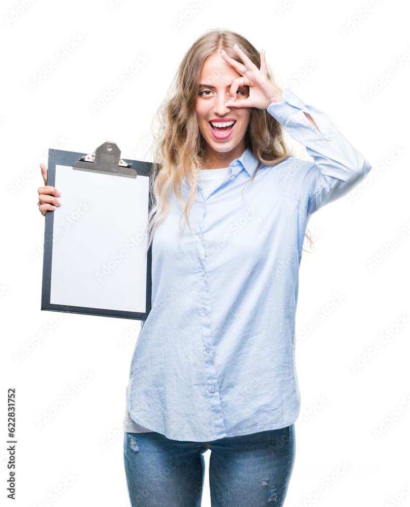 Wall mural Beautiful young blonde business woman holding clipboard over isolated background with happy face smiling doing ok sign with hand on eye looking through fingers