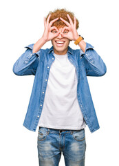 Young handsome man with afro hair wearing denim jacket doing ok gesture like binoculars sticking tongue out, eyes looking through fingers. Crazy expression.