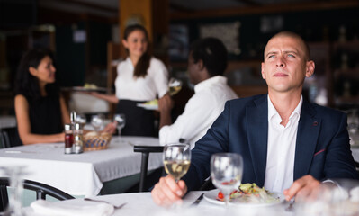 Portrait of young thoughtful businessman resting and having dinner in cozy restaurant