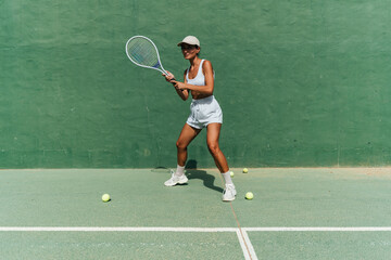 beautiful girl in a cap plays tennis on the tennis court against the background of a green wall