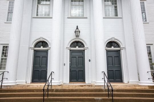 Front of Cheshire town church building with staircase and three black doors with transoms and tall white column pillars 