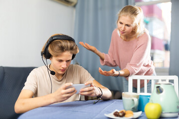 Obraz na płótnie Canvas Teenage boy absorbed in online game on mobile phone, ignoring frustrated mother talking to him. Concept of phubbing and internet gaming addiction