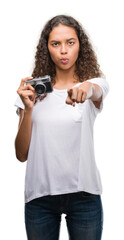 Young hispanic woman taking pictures using vintage camera pointing with finger to the camera and to you, hand sign, positive and confident gesture from the front