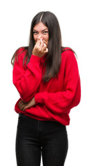Young beautiful hispanic wearing red sweater smelling something stinky and disgusting, intolerable smell, holding breath with fingers on nose. Bad smells concept. - obrazy, fototapety, plakaty