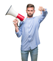 Young handsome man yelling through megaphone over isolated background with angry face, negative sign showing dislike with thumbs down, rejection concept