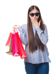 Young Chinese woman over isolated background holding shopping bags on sales cover mouth with hand shocked with shame for mistake, expression of fear, scared in silence, secret concept
