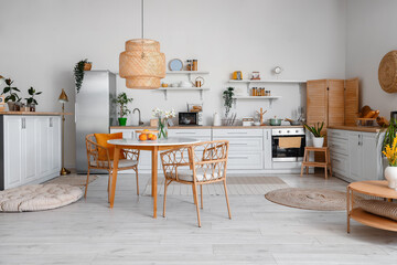 Interior of light kitchen with stylish fridge, counters, table and chairs