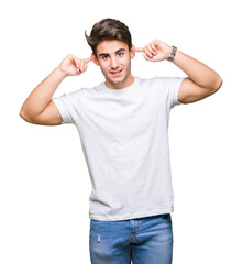 Fototapeta premium Young handsome man wearing white t-shirt over isolated background Smiling pulling ears with fingers, funny gesture. Audition problem