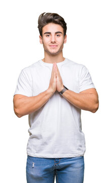 Young handsome man wearing white t-shirt over isolated background praying with hands together asking for forgiveness smiling confident.