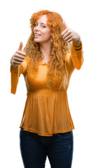 Young redhead woman approving doing positive gesture with hand, thumbs up smiling and happy for success. Looking at the camera, winner gesture.