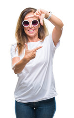 Middle age hispanic woman wearing fashion sunglasses over isolated background smiling making frame with hands and fingers with happy face. Creativity and photography concept.