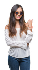 Young asian woman wearing sunglasses over isolated background smiling with happy face looking and pointing to the side with thumb up.