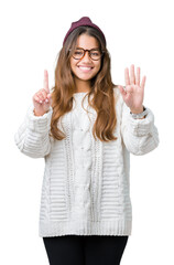 Young beautiful brunette hipster woman wearing glasses and winter hat over isolated background showing and pointing up with fingers number six while smiling confident and happy.