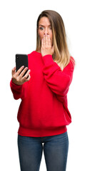 Naklejka premium Beautiful young woman using smartphone cover mouth with hand shocked with shame for mistake, expression of fear, scared in silence, secret concept