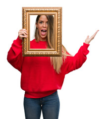 Fototapeta premium Beautiful young woman holding vintage frame very happy and excited, winner expression celebrating victory screaming with big smile and raised hands