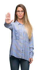 Beautiful young woman wearing elegant shirt and glasses doing stop sing with palm of the hand. Warning expression with negative and serious gesture on the face.
