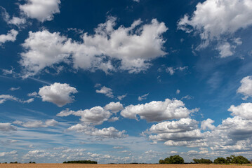 Zerzauste Cumulus- oder Schönwetterwolken am Himmel mit einem Feld und einer Windkraftanlage im...