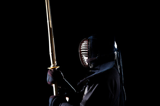 Side view of person playing fencing against dark background
