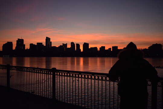 Fototapeta Silhouette of person looking over city  across body of water at sunset