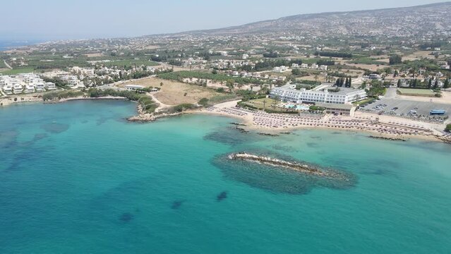 Corallia Beach on the island of Cyprus, located in the town of Peja near Paphos. A bird's-eye view captures the stunning, pristine blue waters of the Mediterranean Sea. 