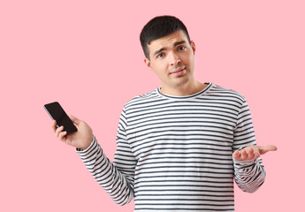 Helpless young man with smartphone on pink background