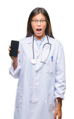 Young asian doctor woman holding smartphone over isolated background scared in shock with a surprise face, afraid and excited with fear expression