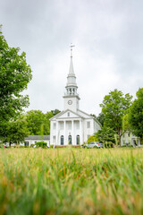 View from the grass of the front exterior of white New England church building on Cheshire green in...