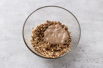 Glass bowl with a mixture of oatmeal, nuts, coconut sugar, dates and linseed egg on a gray textured background, top view. Cooking vegan healthy oatmeal cookies