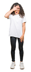 Obraz premium Young beautiful woman with curly hair wearing white t-shirt peeking in shock covering face and eyes with hand, looking through fingers with embarrassed expression.