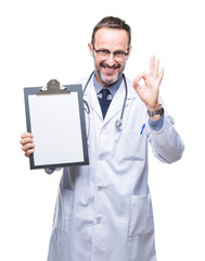 Middle age senior hoary doctor man holding clipboard isolated background doing ok sign with fingers, excellent symbol