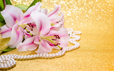 Fototapeta na wymiar White lilies and pearl necklace on a shiny gold background 
