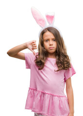 Brunette hispanic girl wearing easter rabbit ears with angry face, negative sign showing dislike with thumbs down, rejection concept