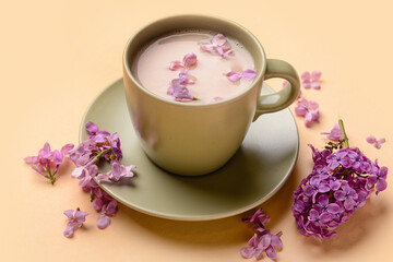 Cup of coffee and beautiful lilac flowers on beige background, closeup
