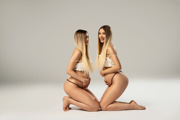 Photo of two beautiful pregnant twins sisters posing together in studio. A lot of copy space. Mothers. Family. - obrazy, fototapety, plakaty