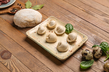 Plate with uncooked dumplings and ingredients on wooden background
