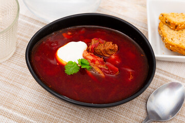 Delicious traditional Ukrainian, Russian vegetable beetroot soup with beef decorated by sour cream and herbs served on black plate