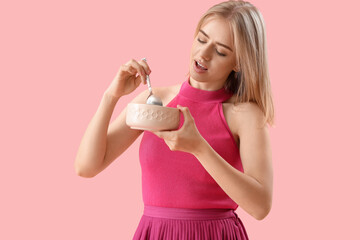 Young woman with spoon and bowl on pink background