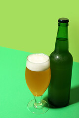 Bottle and glass of cold beer on green background
