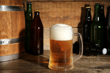 Mug of cold beer with bottles and barrel on wooden background, closeup